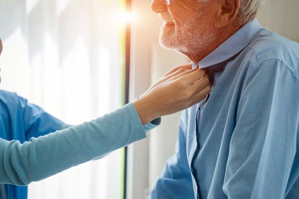 Family member visits an older resident in a bright assisted living common room with photographs and refreshments.